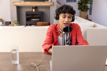Naklejka premium Male with headphones speaking into microphone at living room, table with laptop, copy space