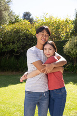 Fototapeta premium Asian couple hugging and smiling in private garden on green lawn under sunlight
