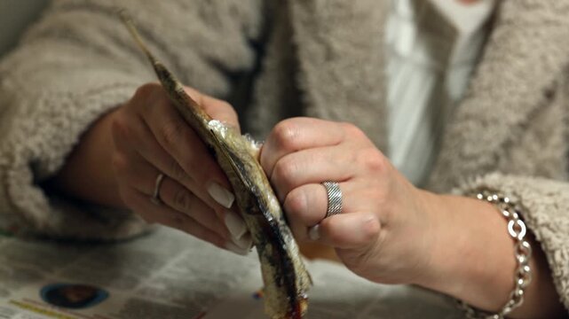 A woman's hands cut up dried raba for eating. A woman cleans dried fish.
