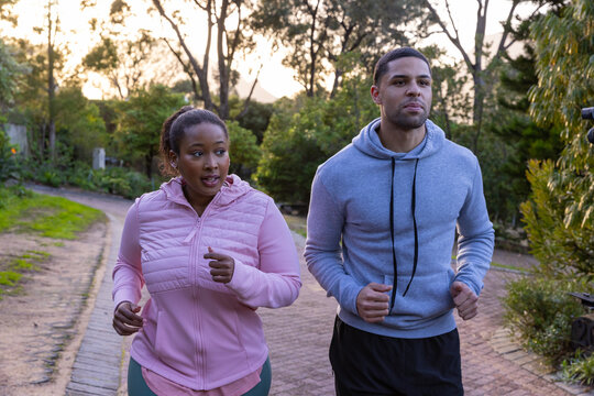 Diverse friends running on brick pathway through leafy park wearing jacket and hoodie