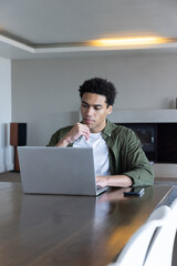 Naklejka premium African american man working on laptop at table in living room with smartphone