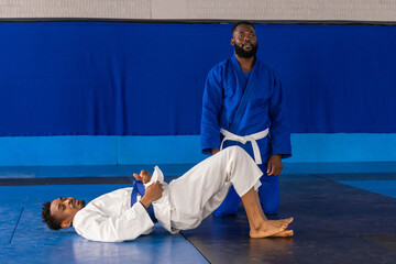 African american male training partners practicing hip bridge in gym in gis, belts on mats