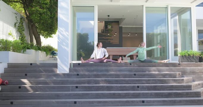 Encouraged by sun warming deck two women stretching straddle splits for improving flexibility