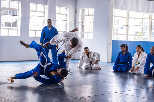 African american men executing judo throw in gis on dojo mats under instructor watch