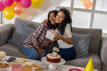 Obraz premium Diverse mom and teenage daughter hugging and celebrating birthday in living room with cake