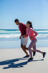 Diverse couple running together on wet shoreline in athletic attire and black running shoes