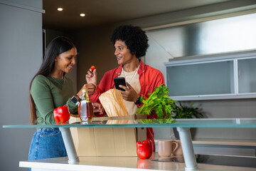 African american and indian couple unpacking groceries in kitchen with grocery bag, smartphone © wavebreak3