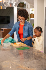 Fototapeta premium Diverse mother with daughter preparing sandwich with carrots, container lid on kitchen island
