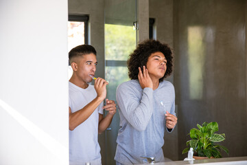 Fototapeta premium Diverse male friends brushing teeth at bathroom counter with toothbrushes, soap dispenser and plant