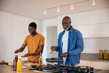 African american father and son cooking breakfast at kitchen island using frying pan, spatula
