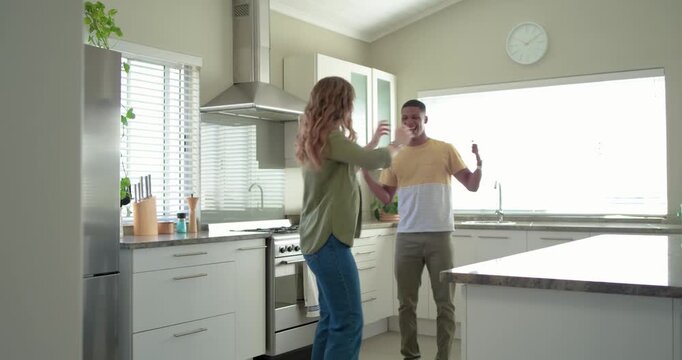 Couple playfully dancing in kitchen man entering from doorway mirroring woman's steps by island