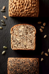 Thick slices of golden seeded bread with nuts and grains on dark slate background