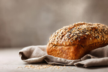 Freshly baked golden multigrain bread loaf topped with oats and seeds on linen cloth, warm steam rising