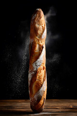Tall French baguette standing vertically with flour dust falling, crisp golden crust on dark wooden table