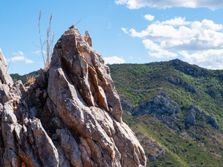 Fototapeta premium A rocky outcrop is visible in the foreground with green hills and a blue sky filled with clouds in the background. The scene shows a natural environment during daytime