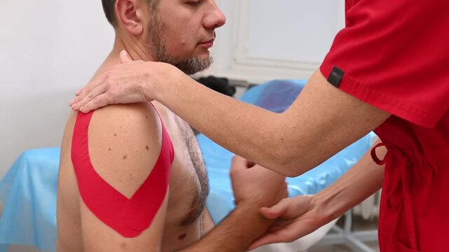 An alternative medicine doctor applies kinesio tape to a male patient's shoulder for back and neck pain, kinesiotherapy ,  posture check, spine health, back care, orthopedic prevention