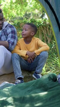 Vertical video: Pointing father drawing son in mustard shirt gazing to see sky at tent, green bag