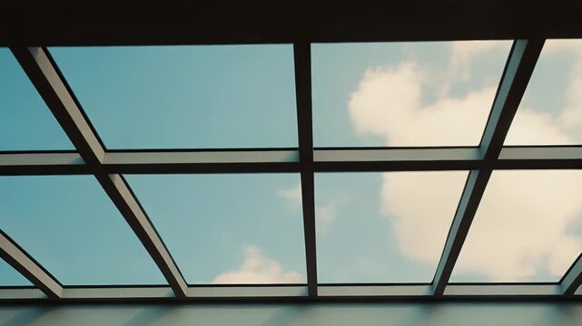 Looking through a contemporary ceiling window, the view features a bright blue sky with white clouds, showcasing architectural design and bringing natural light into an interior space