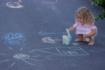 Little girl putting colorful chalks into a bucket on the asphalt with drawings