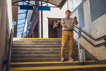 Senior man is standing at railway station and talking on mobile phone. He is distraught. Senior people traveling.