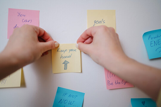 Hand placing motivational sticky notes with positive affirmations on wall