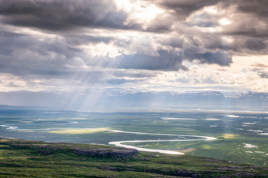 Dramatic shafts of light illuminate glacial river winding through Iceland valley