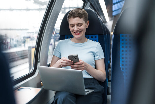 Woman using mobile and laptop in train compartment during commute