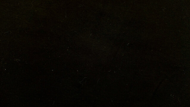 closeup black corduroy fabric texture with white lint fibers and subtle dust specks in dim moody lighting evoking mysterious abstract pattern