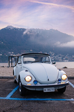 COMO, ITALY - DECEMBER 15, 2025: Side and front views of a classic white VW Beetle (Type 1) cabriolet parked near the shore of Lake Como at sunset.