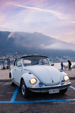COMO, ITALY - DECEMBER 15, 2025: Side and front views of a classic white VW Beetle (Type 1) cabriolet parked near the shore of Lake Como at sunset.