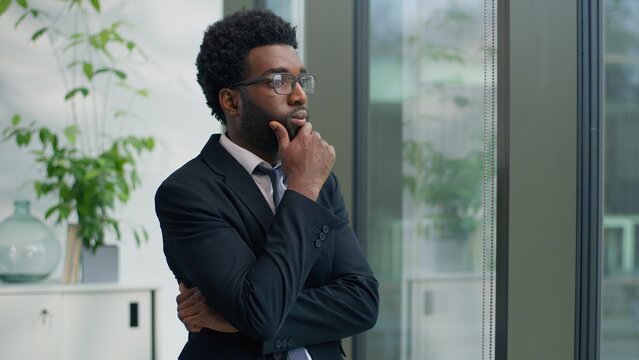 Hesitate creative thoughtful African American man business male entrepreneur businessman thinking idea startup corporate solution serious look at window looking in office manager job pondering decide