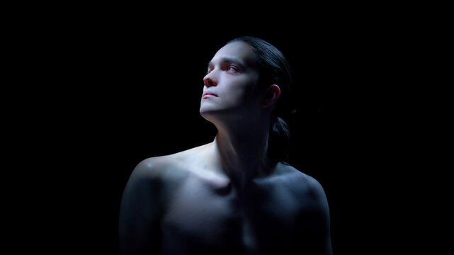 Male upper body portrait with upward gaze on black background. Concept of psychological resilience themes, wellness branding, aesthetic medicine visuals, and contemporary editorial design.