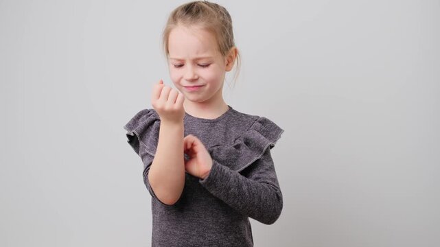 Portrait of sad unhealthy little school girl scratching an itch with hand, isolated on white background. Kid suffers from allergy. Sensitive skin, food allergy symptoms, irritation