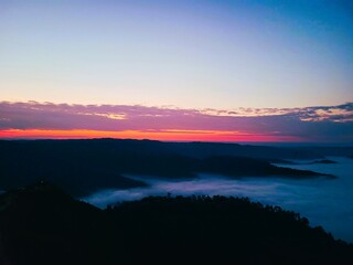 Fototapeta premium Vibrant Pink and Orange Dawn Sky over a Dense Sea of Clouds Submerging the Valley Floor at Nongjrong, Meghalaya, India