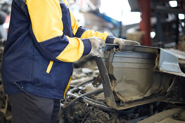 Mechanic is working in a workshop setting with a car that has been damaged