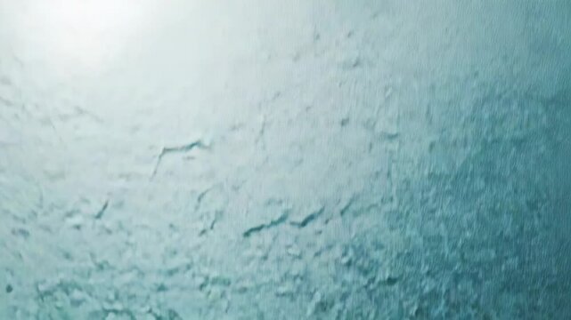 Textured glass creating an abstract background, featuring rough, uneven patterns and a cool blue green gradient from bright transparency to darker, opaque areas