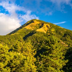 Obraz premium Green mountain rises under a sky with clouds, offering scenic view, in natural landscape