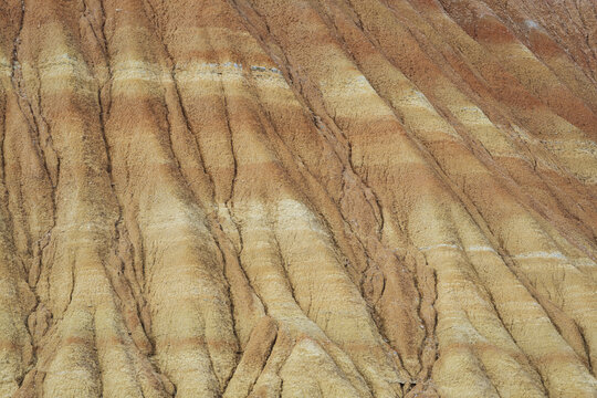 View of arid badlands carved by time and weather, with striated layers of ochre, tan, and cream creating a textured, almost otherworldly landscape, Bardenas Reales, Navarre, Spain.