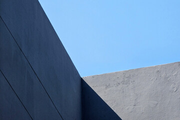 Abstract minimalist architecture of dark gray concrete wall with strong geometric lines against blue sky.