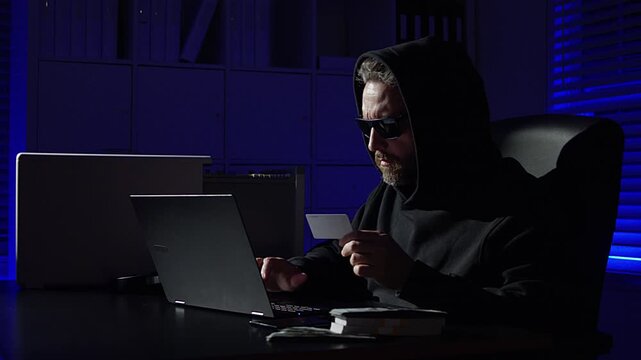 hacker typing code in dark office. Masked hacker hacking a computer in night room. Night hacker attack network security. Cyber hacker and data security. Digital credit card fraud.