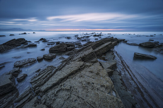 View of jagged rocks meet the tranquil sea under a serene sky, a dance of stone and water at twilight, Ugeraga, Basque Country, Spain.