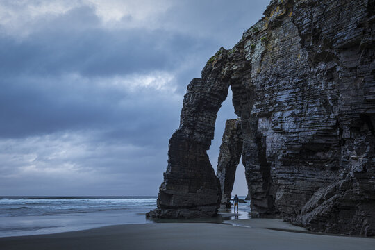 View of cathedral-like arches sculpted by time and tide stand majestically on the sandy shore under a brooding sky, Ribadeo, Lugo, Spain.