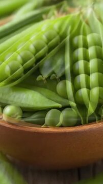 A vibrant close-up captures an abundance of fresh green peas nestled within their pods, artfully arranged in a rustic wooden bowl. Several pods are split open, revealing rows of glossy, perfectly roun