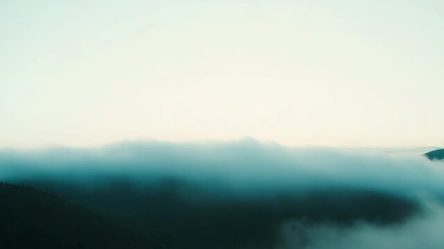 Dense fog covers an expansive natural mountain landscape, creating a tranquil cloud inversion with distant tree covered peaks emerging from the misty atmosphere