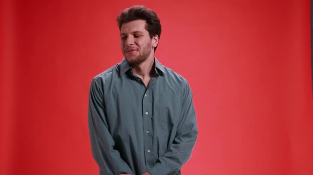 Shy smiling man looking down on red studio background. Concept of modest happiness, quiet joy, emotional relief, positive reaction, sincerity, natural human emotion.