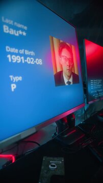 Vertical shot of cyberpunk man wearing smart LED visor stealing passports data of users while hacking on computer in dark futuristic workspace