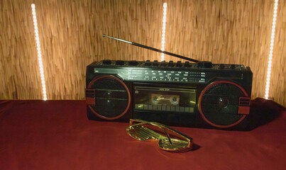 Old boombox and gold sunglasses placed on a red fabric surface in a dimly lit room