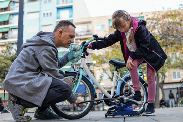 Obraz premium Father and nine year old child pumping wheels of a kid's bicycle outdoors, family activity and childhood