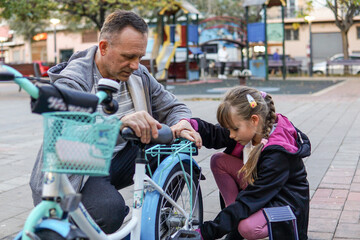 Obraz premium Father and nine year old child pumping wheels of a kid's bicycle outdoors, family activity and childhood