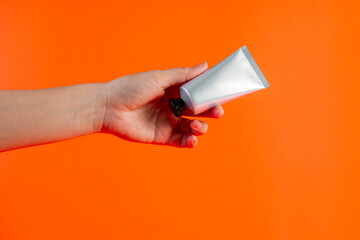 Cosmetics tube against and hand on orange background. 